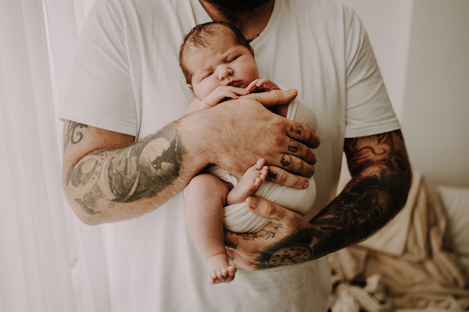 newborn baby being held in arms of tattooed father