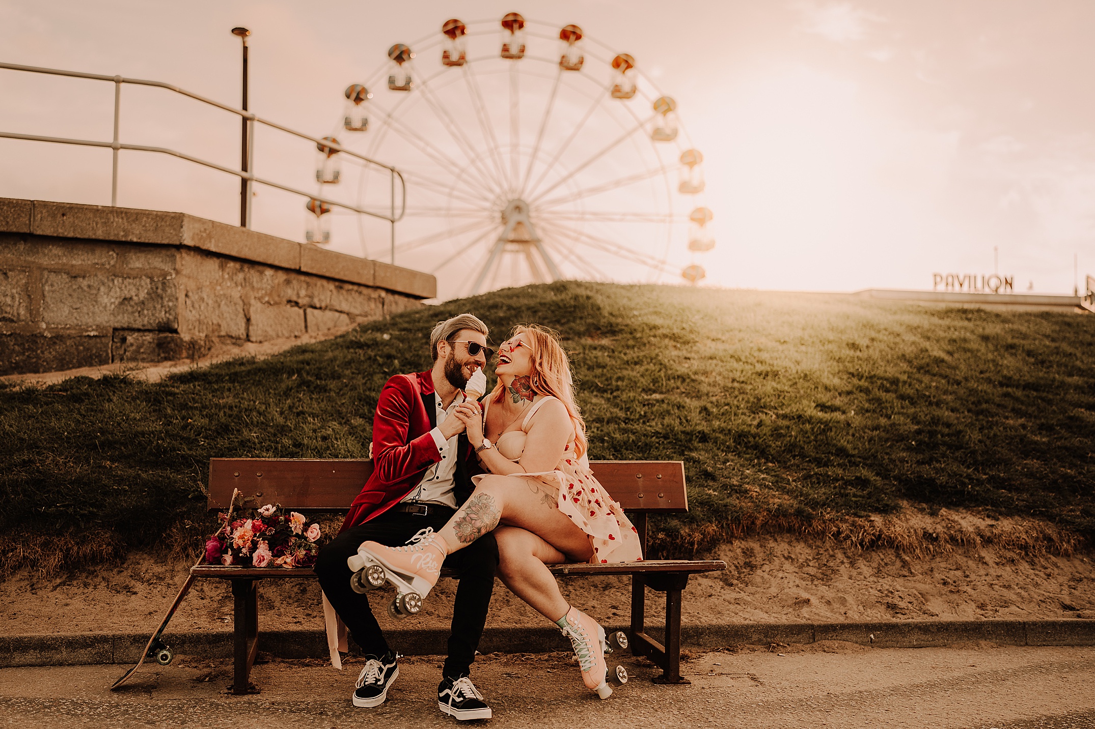 couple sitting on bench eating ice cream and laughing she is wearing roller skates with big wheel in background scotland engagement photos