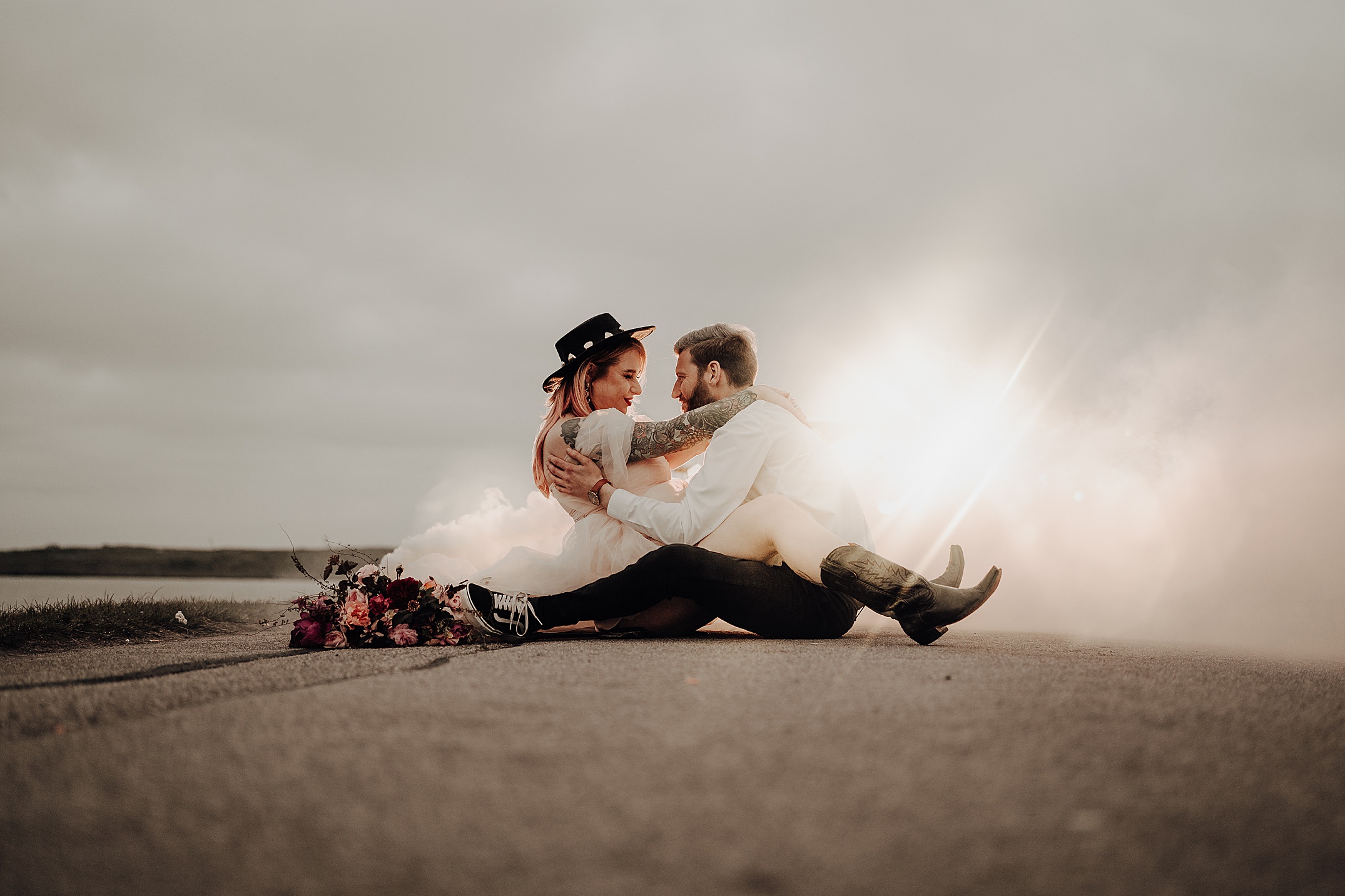 couple hugging facing each other as they sit on road with smokey light in background scotland engagement photos