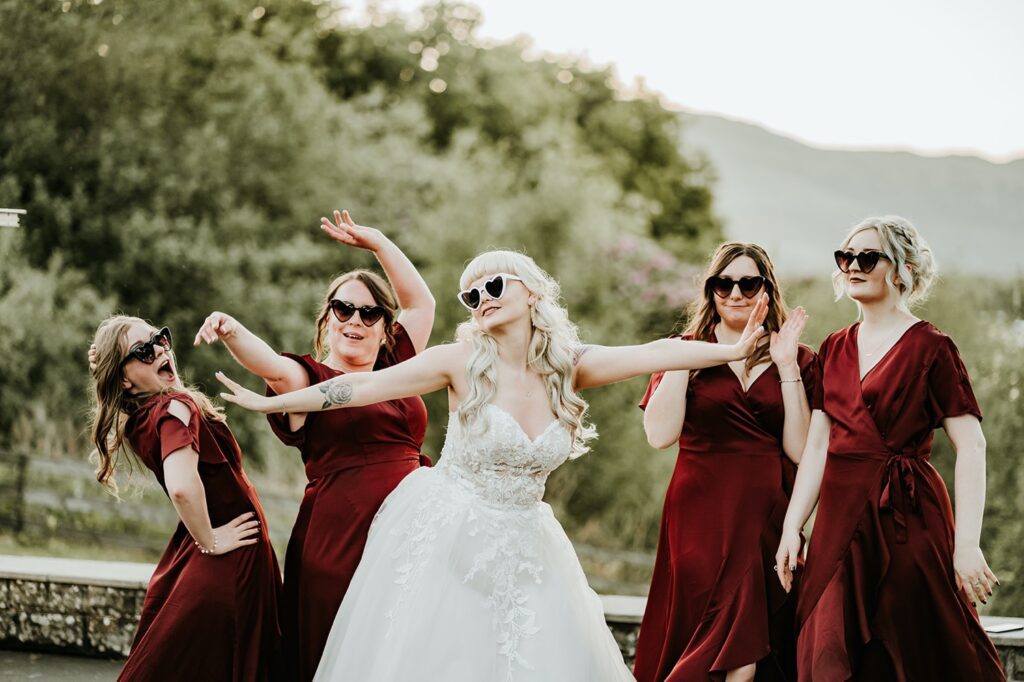 Bride wearing sunglasses posing with bridesmaids in red dresses for group shots