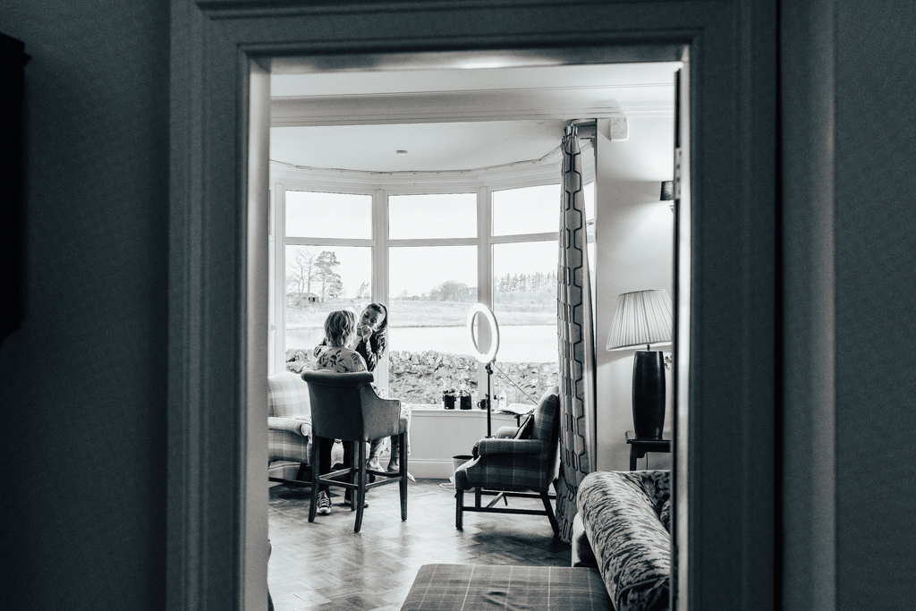 woman sitting in a stool having her make up done in a bay window