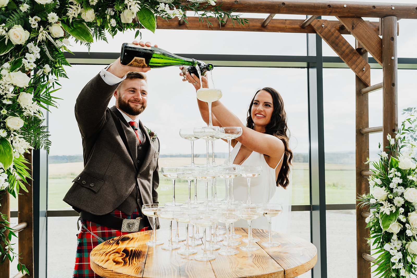 Couple standing behind a champagne tower for their wedding at The Schivas Steading