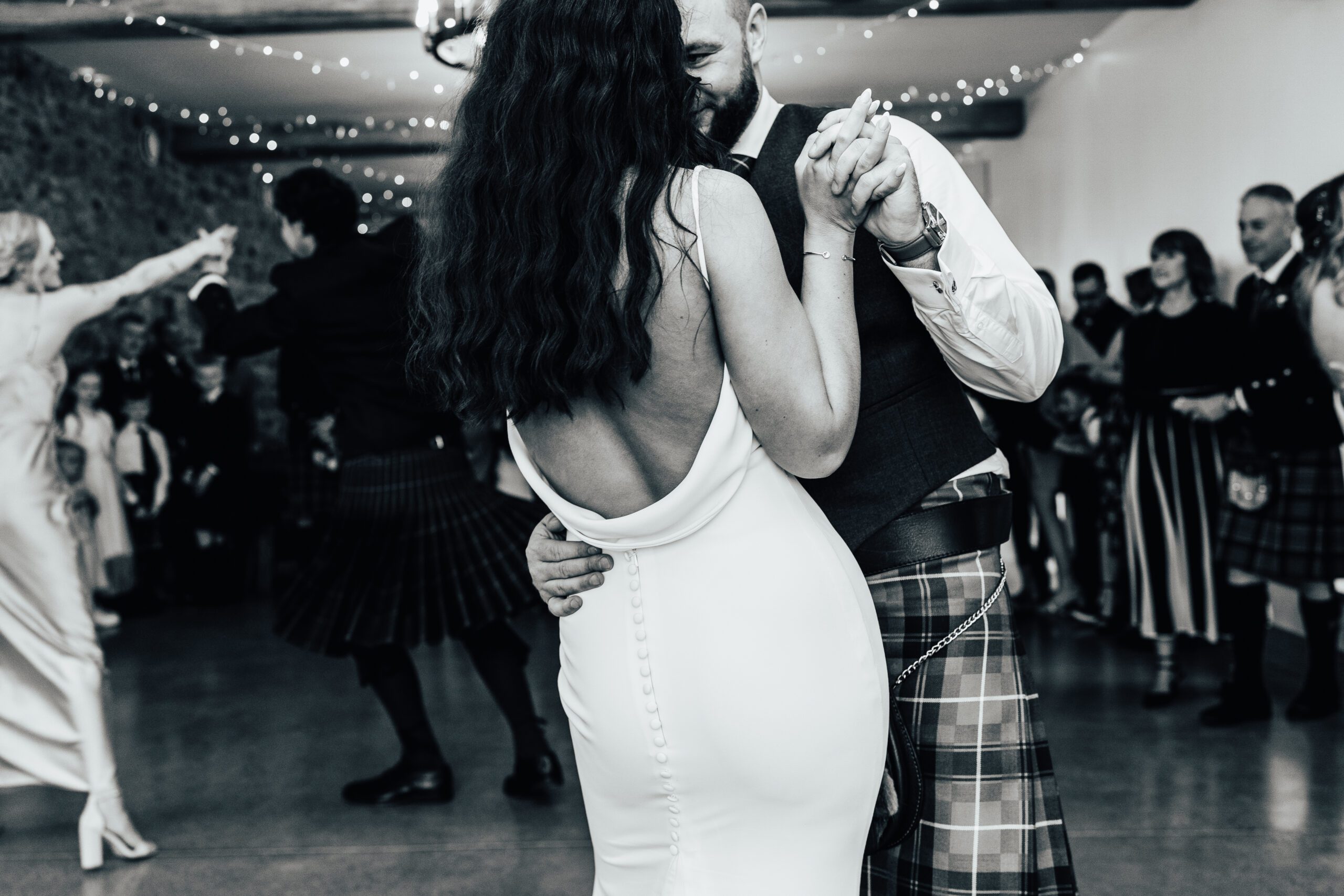 Couple embrace during their first dance on the timeless natural wedding day image shows the back of brides dress
