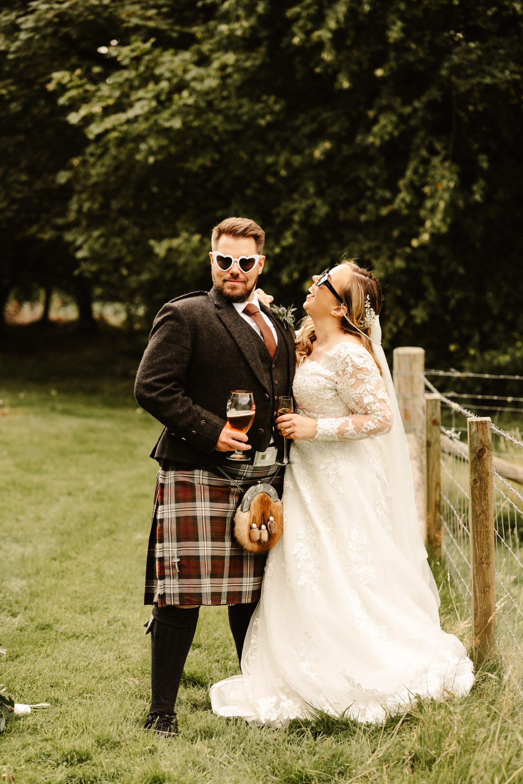 Couple pose on their wedding day wearing heart shaped glasses the couple are laughing on their traditional scottish wedding with a twist
