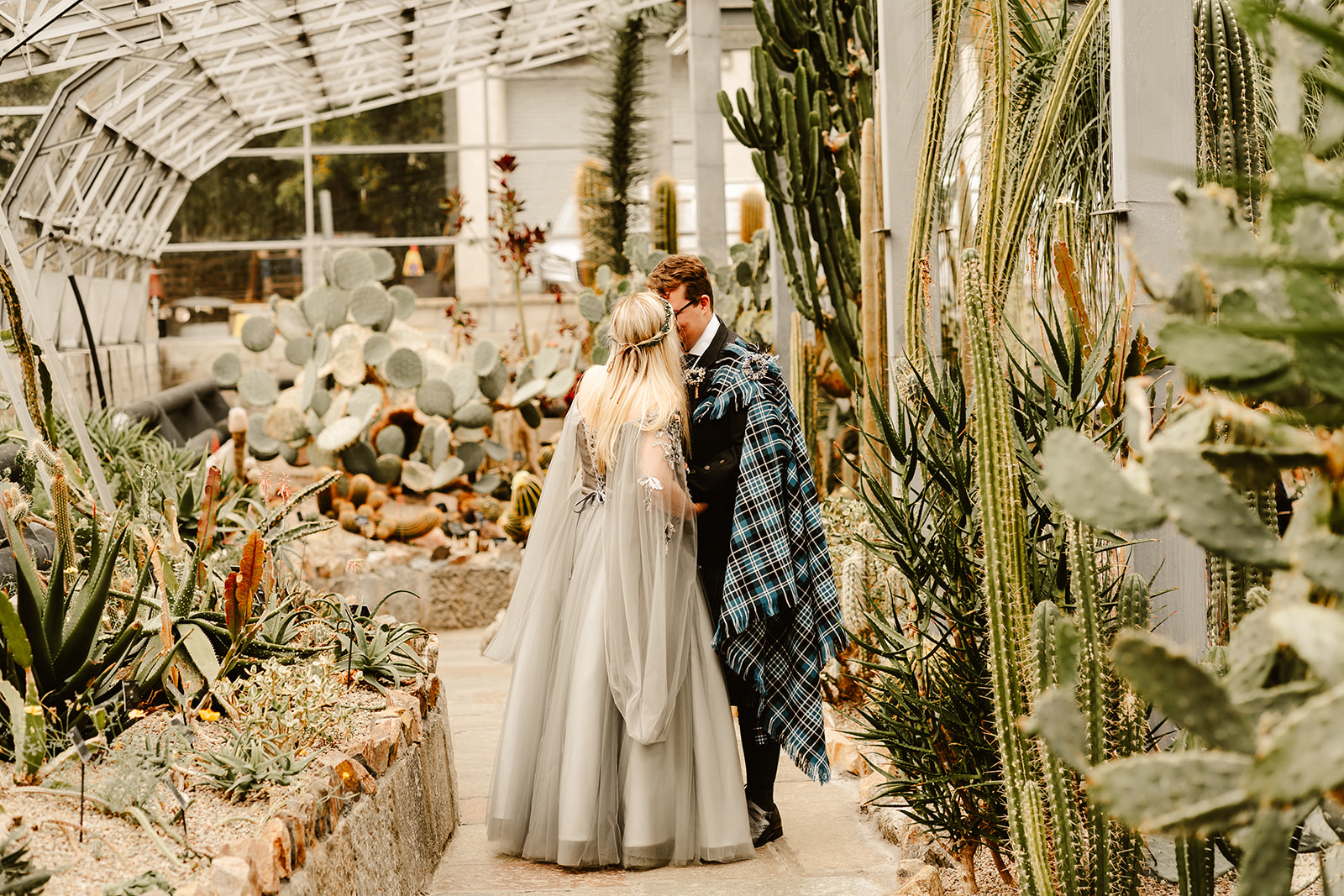 Bride standing in her wedding dress and groom standing between Cacti in Duthie Park Winter Gardens