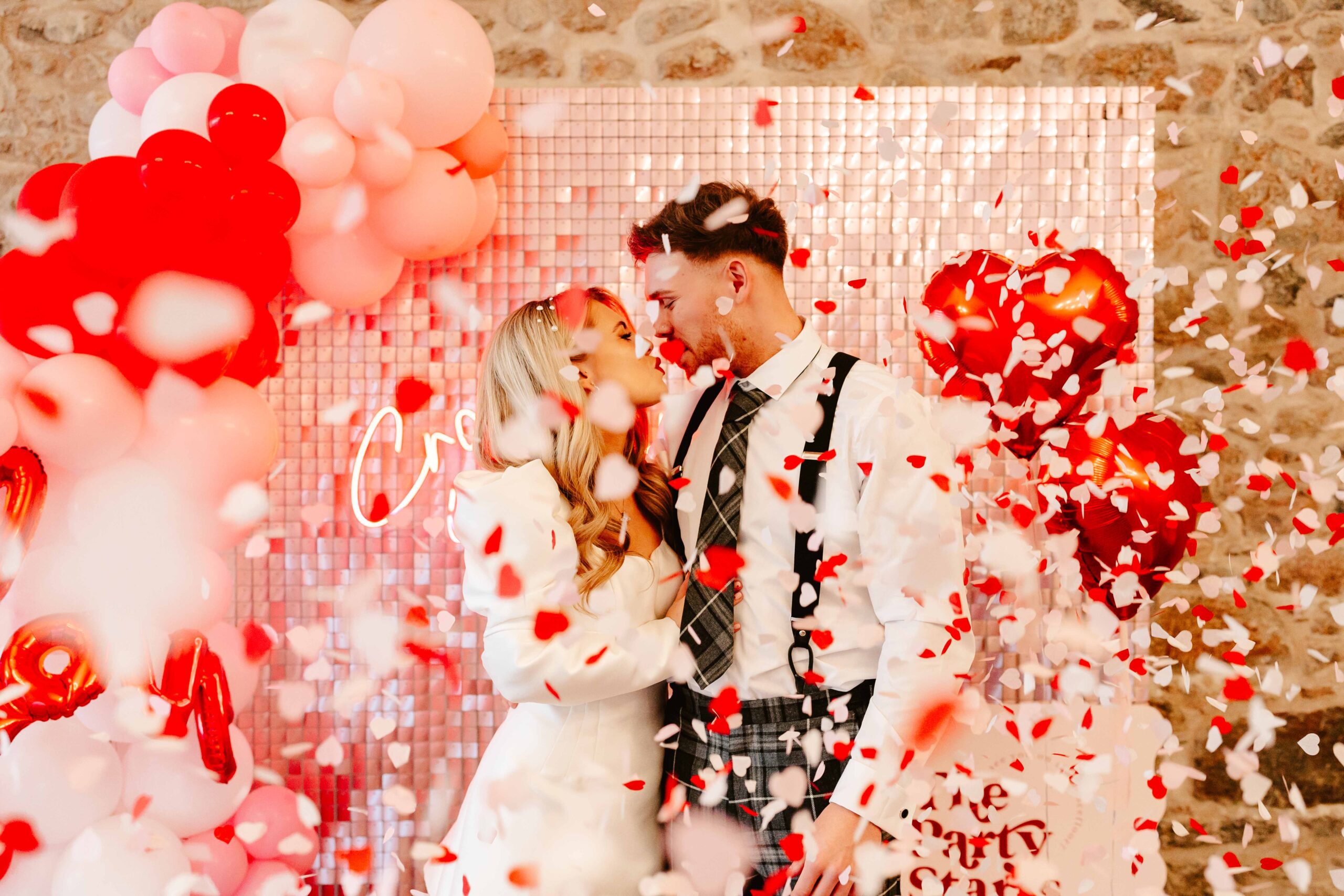 bride and groom kiss in front of pink sequin backdrop as confetti falls on them