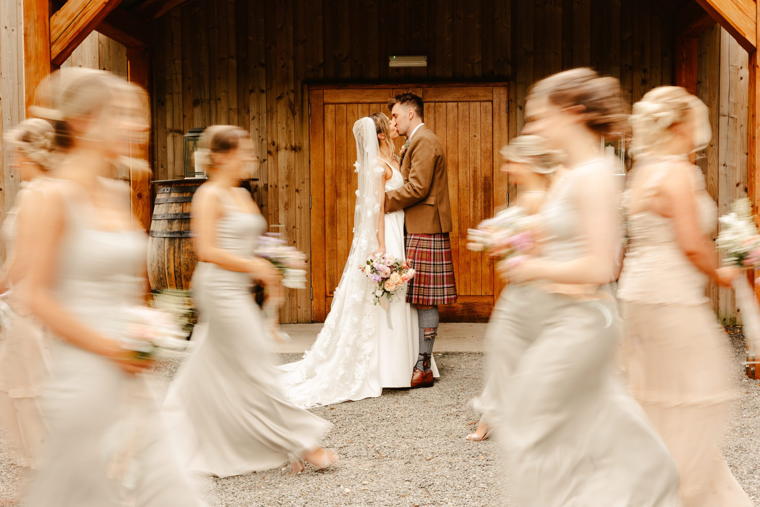 bride and groom kiss at netherdale house wedding while bridal party walk in front photographed with motion blur