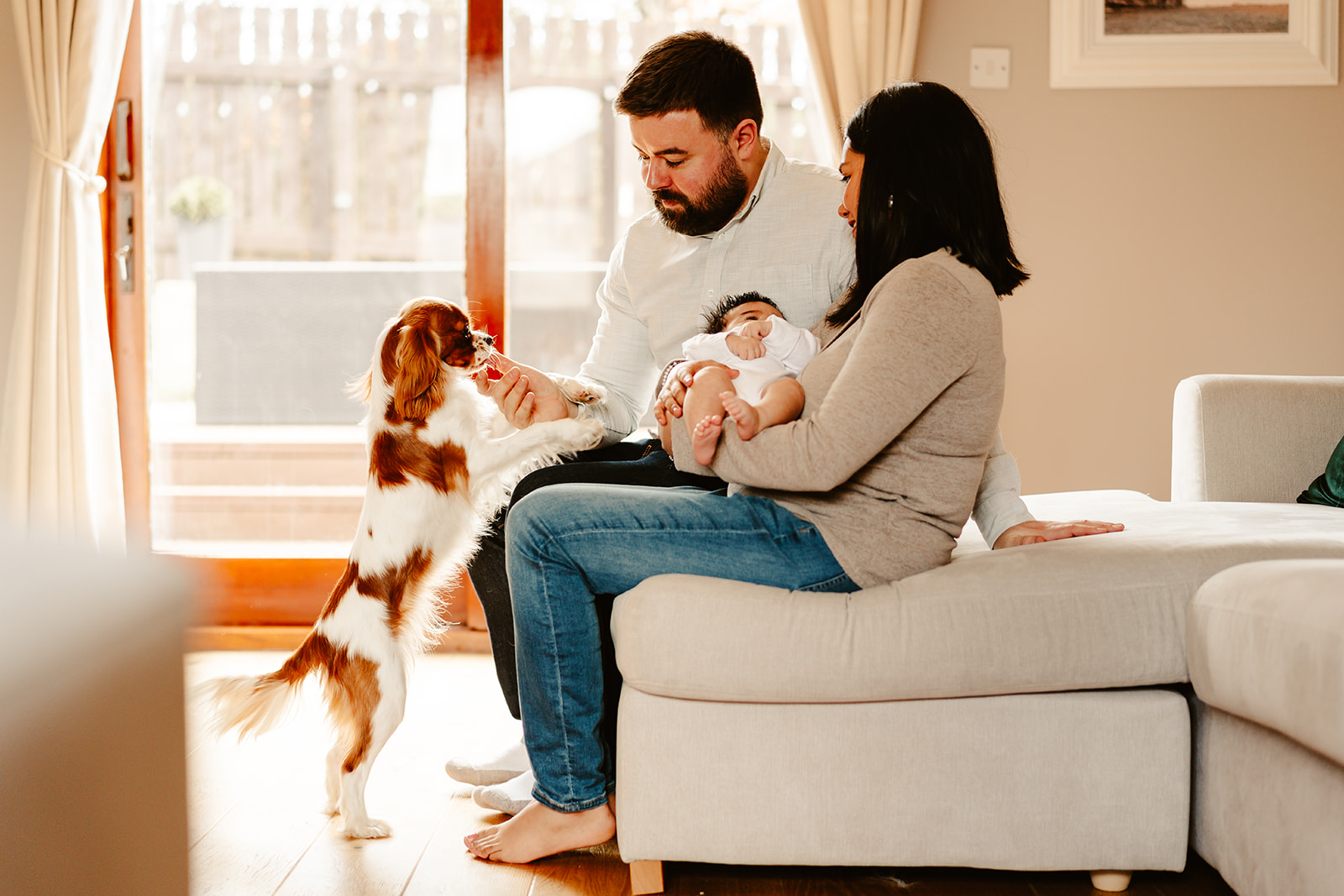 family sit on sofa with dog during newborn photoshoot