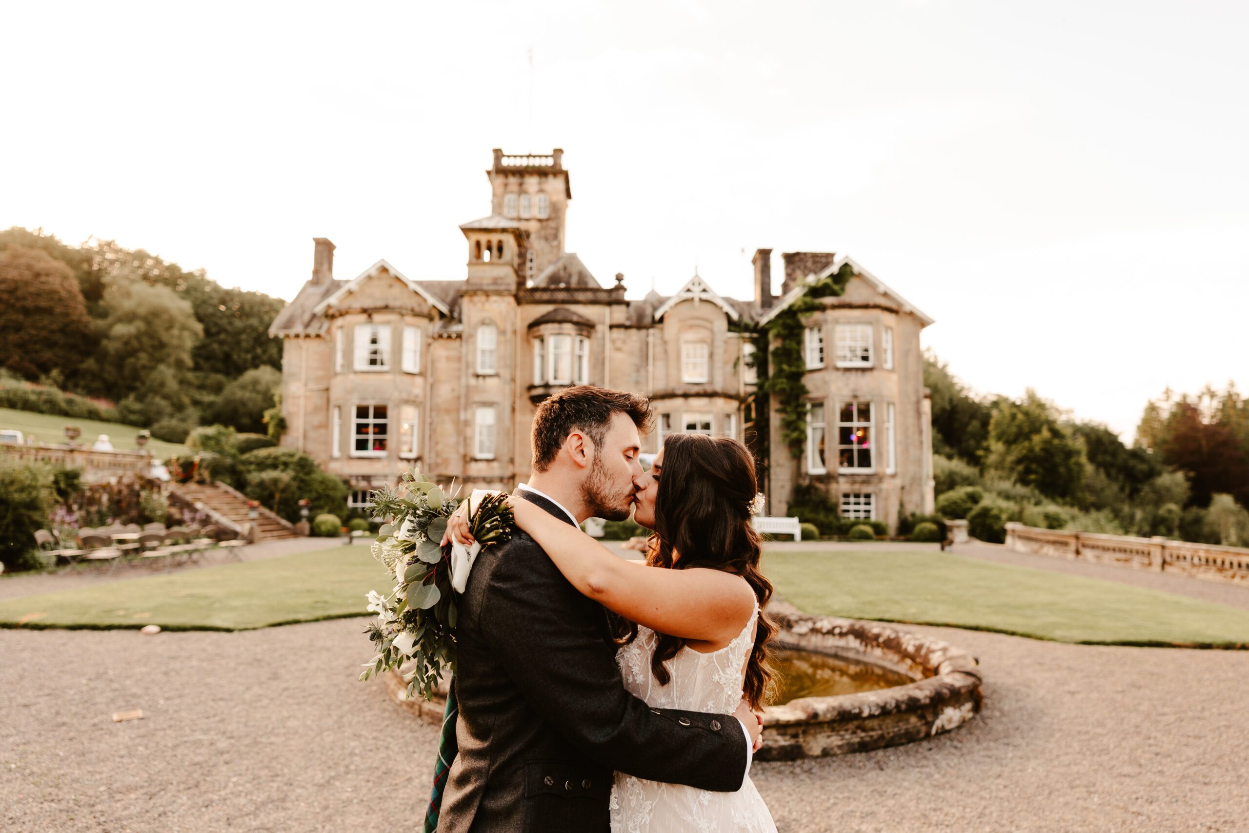 bride and groom kiss infront of rustic scottish wedding castle auchen castle during sunset