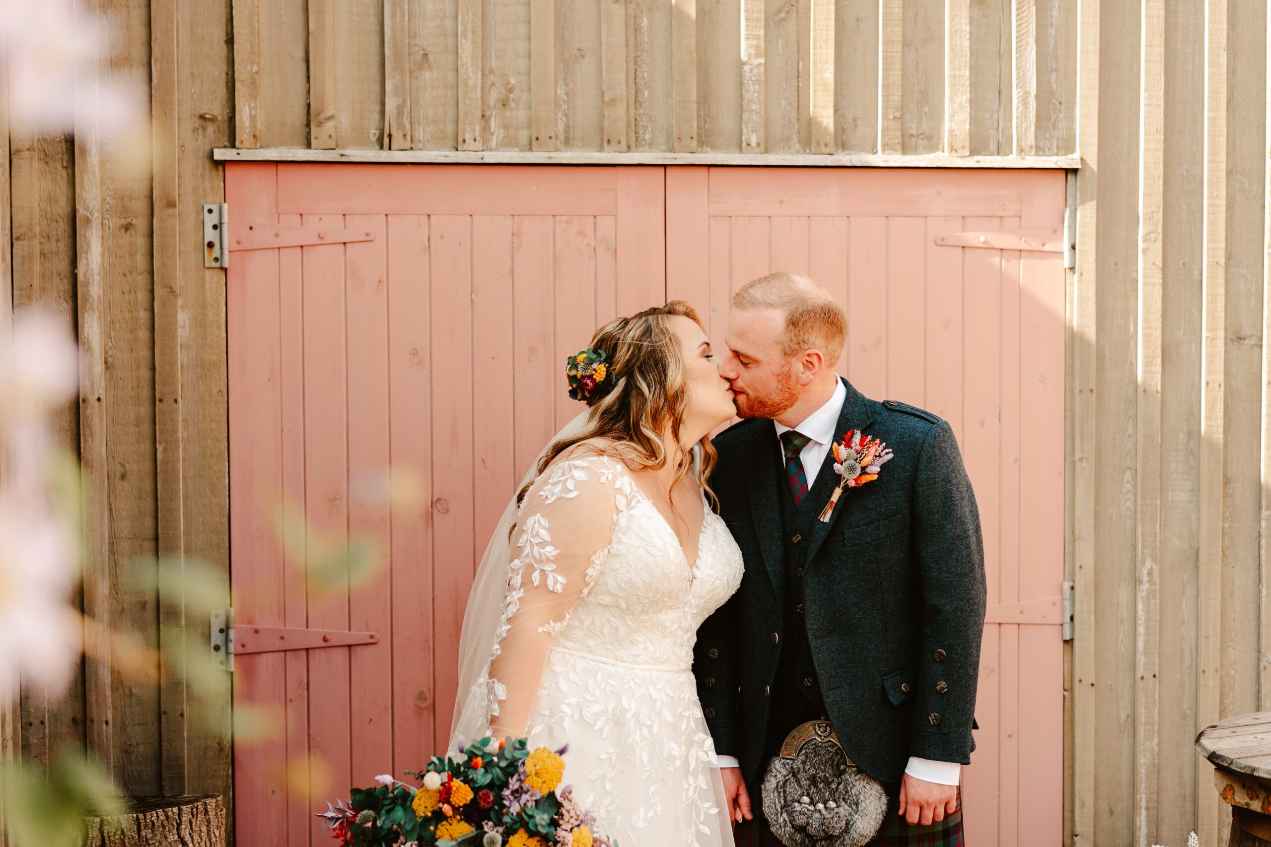 bride and groom share a kiss infront of pink wooden doors, during a banff aberdeenshire wedding